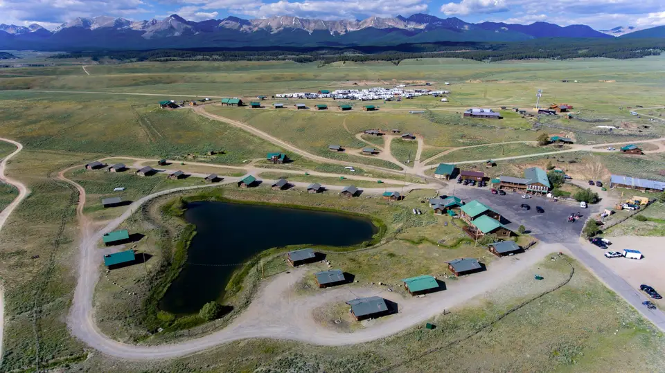 Aerial view of the Trading Post: log cabins around the fishing pond, the RV park beyond, mountains on the horizon